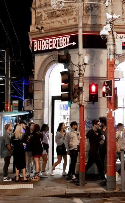 People walking down a street at night outside a burger restaurant